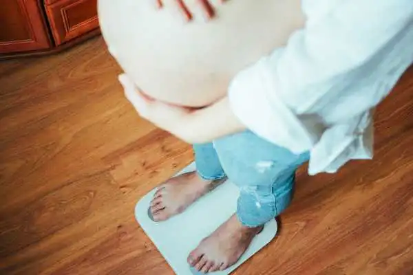 Image of woman weighing herself and experiencing weight gain through pregnancy Westbury